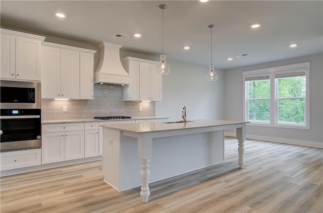 kitchen with appliances with stainless steel finishes, custom exhaust hood, sink, a center island with sink, and white cabinetry