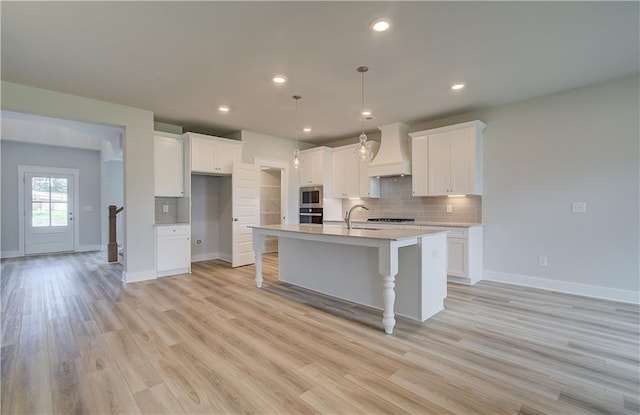 kitchen with white cabinetry, an island with sink, pendant lighting, and custom exhaust hood