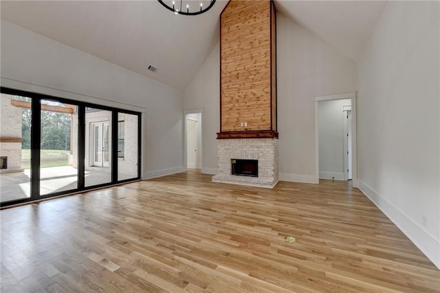 unfurnished living room with an inviting chandelier, a brick fireplace, light hardwood / wood-style floors, and high vaulted ceiling