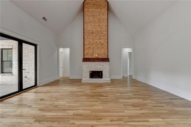 unfurnished living room with high vaulted ceiling, light hardwood / wood-style floors, and a brick fireplace