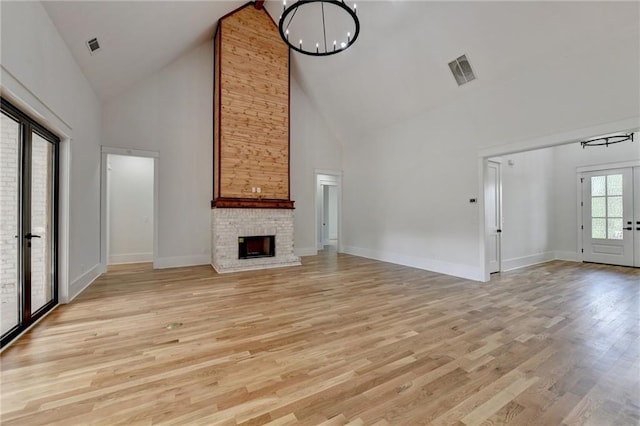 unfurnished living room with an inviting chandelier, high vaulted ceiling, a fireplace, and light hardwood / wood-style floors