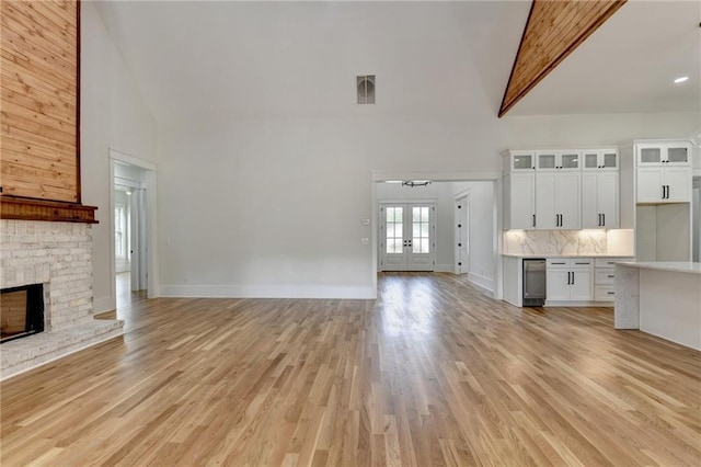 unfurnished living room with french doors, light hardwood / wood-style floors, and high vaulted ceiling