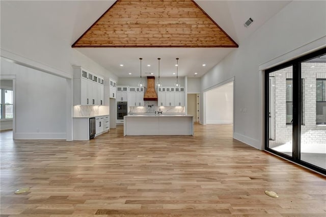 kitchen featuring high vaulted ceiling, decorative light fixtures, white cabinetry, custom range hood, and a center island with sink