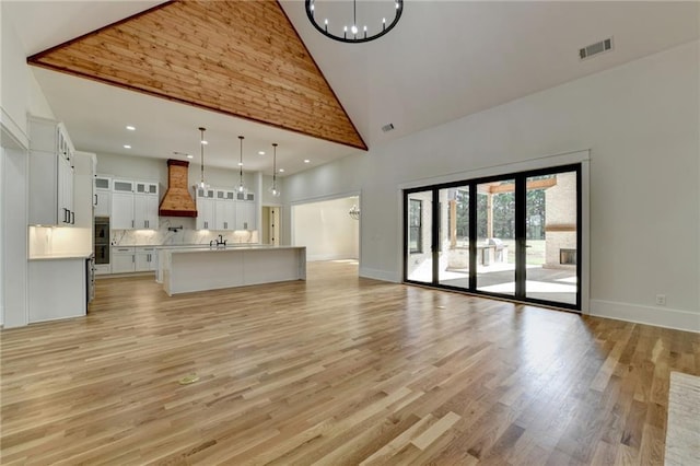 unfurnished living room with an inviting chandelier, sink, high vaulted ceiling, and light hardwood / wood-style flooring