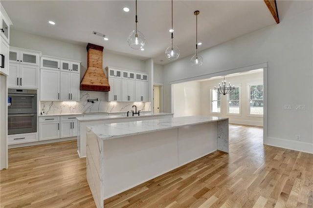 kitchen featuring white cabinetry, hanging light fixtures, double oven, and custom range hood