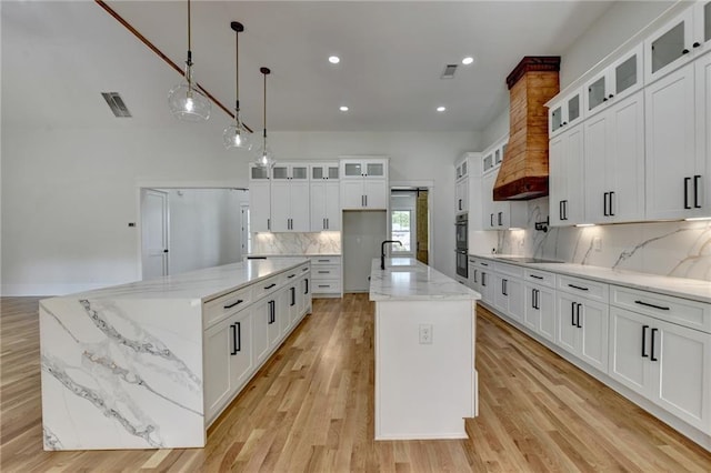 kitchen with a kitchen island with sink, white cabinets, and decorative light fixtures