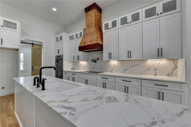 kitchen featuring sink, white cabinetry, light stone counters, a barn door, and black appliances