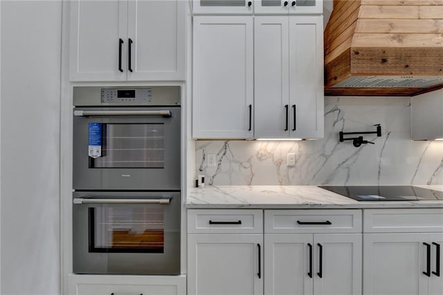 kitchen with double oven, white cabinets, decorative backsplash, black electric stovetop, and light stone counters