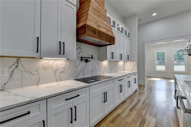 kitchen featuring custom exhaust hood, white cabinetry, light stone counters, hanging light fixtures, and black electric cooktop