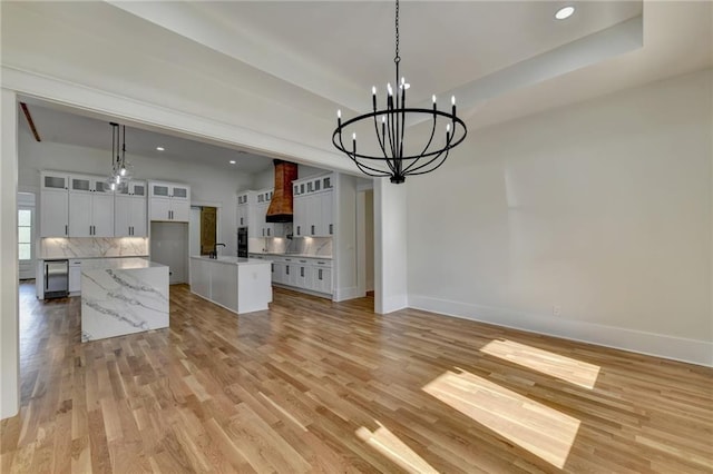 interior space featuring white cabinetry, a tray ceiling, a kitchen island, pendant lighting, and light hardwood / wood-style floors