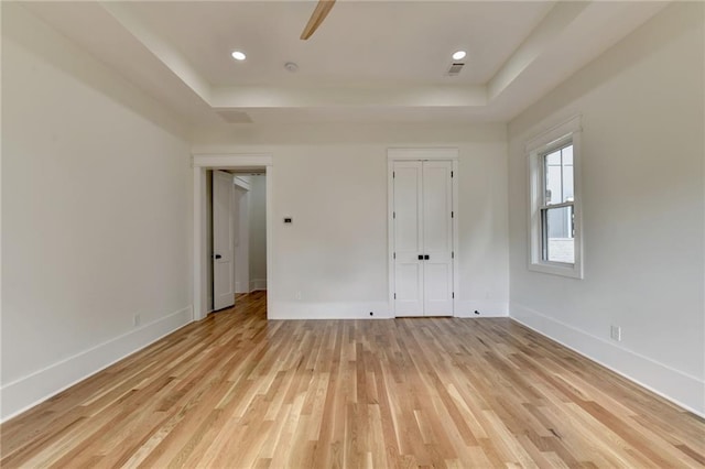 unfurnished bedroom featuring a tray ceiling and light wood-type flooring