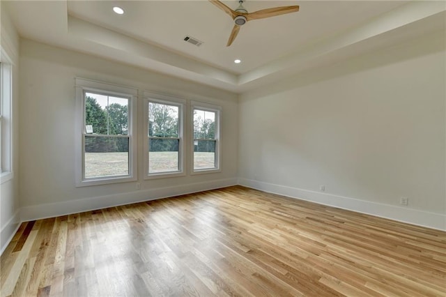 unfurnished room featuring ceiling fan, a tray ceiling, and light hardwood / wood-style flooring