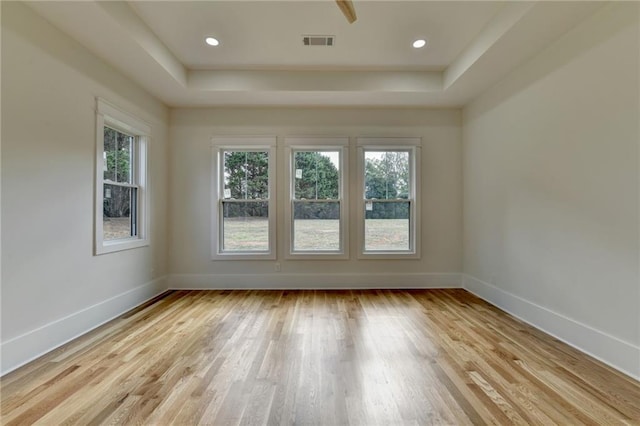 empty room with a tray ceiling and light hardwood / wood-style floors