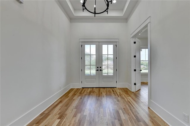 doorway featuring a chandelier, a raised ceiling, french doors, and light wood-type flooring