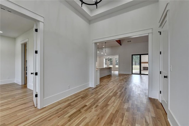 unfurnished living room featuring light hardwood / wood-style flooring, a chandelier, and a high ceiling