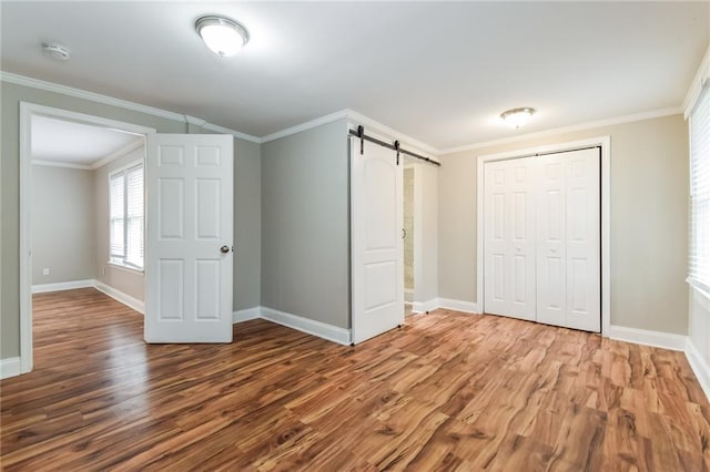 unfurnished bedroom with a barn door, crown molding, a closet, and wood-type flooring