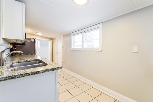 kitchen with stainless steel refrigerator, sink, light stone counters, light tile patterned flooring, and white cabinets