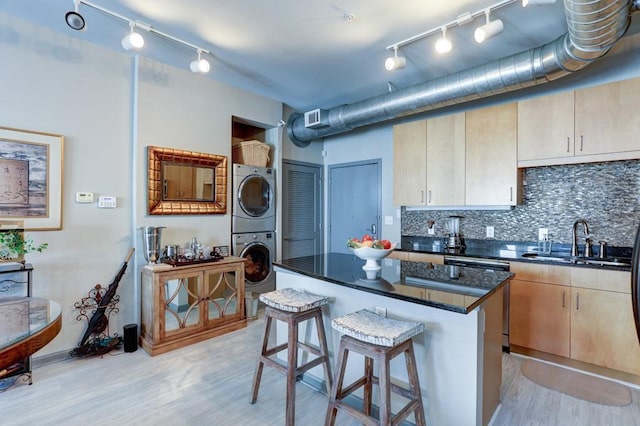 kitchen featuring stacked washer and dryer, tasteful backsplash, dark stone counters, a kitchen island, and sink