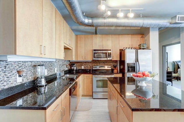 kitchen with dark stone countertops, stainless steel appliances, backsplash, and light brown cabinetry