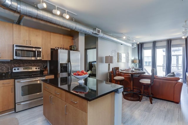 kitchen with dark stone countertops, light wood-type flooring, a kitchen island, stainless steel appliances, and tasteful backsplash