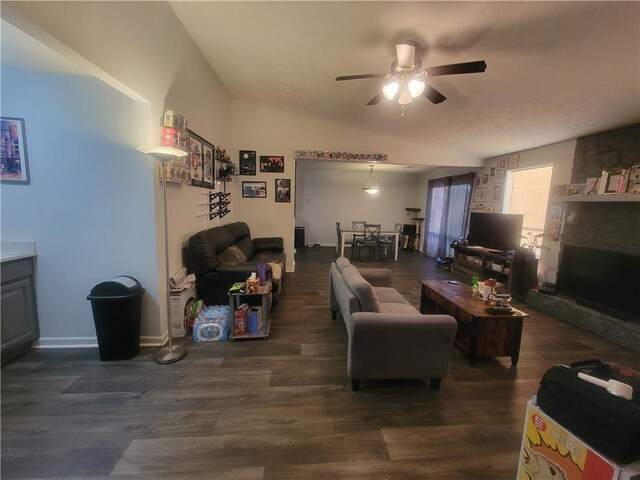 living room featuring dark hardwood / wood-style flooring, vaulted ceiling, a stone fireplace, and ceiling fan