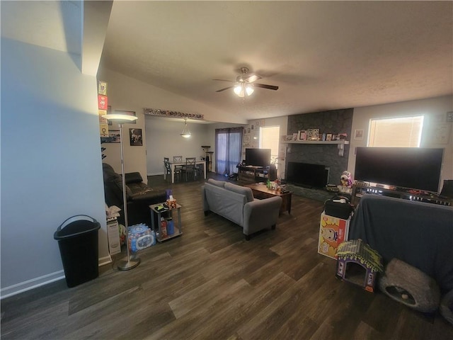 living area featuring a ceiling fan, lofted ceiling, a stone fireplace, dark wood-type flooring, and a textured ceiling