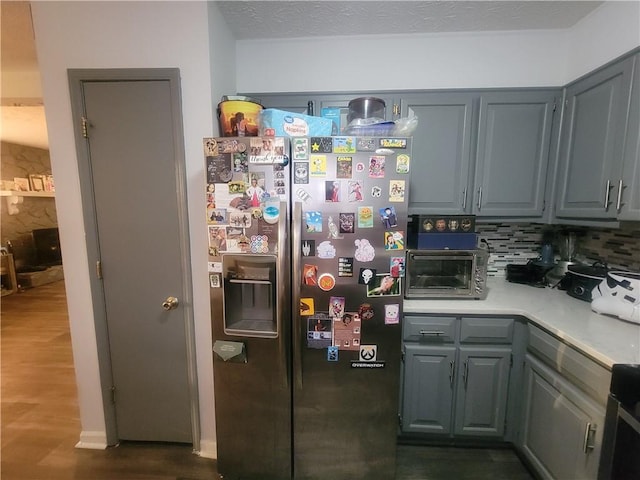 kitchen with a toaster, stainless steel fridge with ice dispenser, gray cabinets, light countertops, and tasteful backsplash