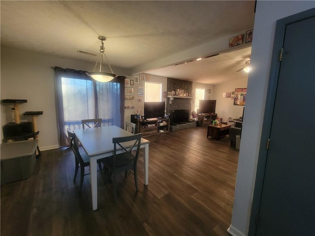 dining room featuring visible vents, vaulted ceiling, a stone fireplace, dark wood-style floors, and a textured ceiling