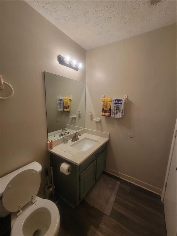 half bath featuring toilet, a textured ceiling, wood finished floors, baseboards, and vanity