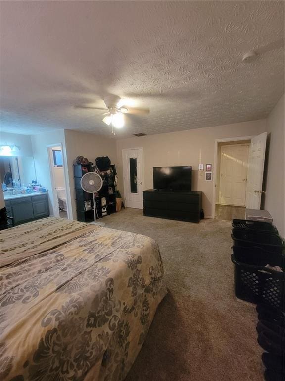 bedroom featuring a textured ceiling, ensuite bath, carpet, and a ceiling fan