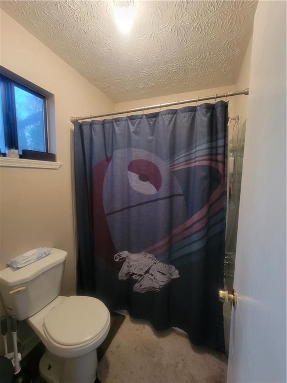 bathroom with walk in shower, toilet, and a textured ceiling