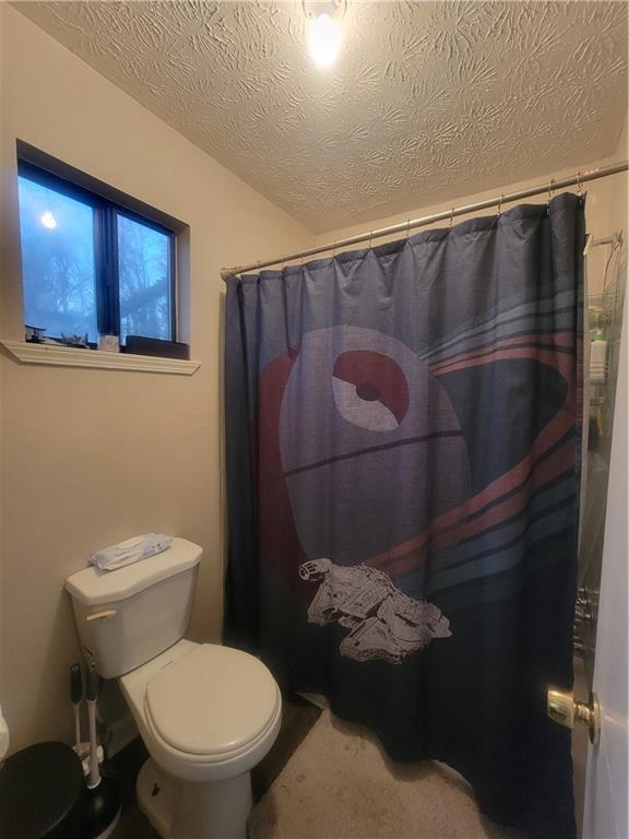 bathroom with shower / tub combo with curtain, toilet, and a textured ceiling