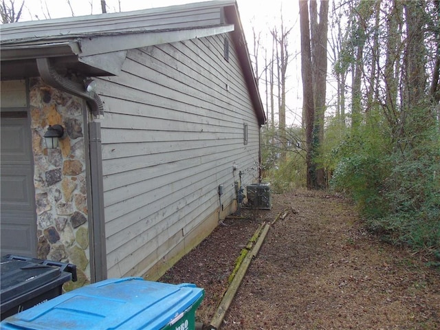 view of home's exterior with a garage, stone siding, and central air condition unit