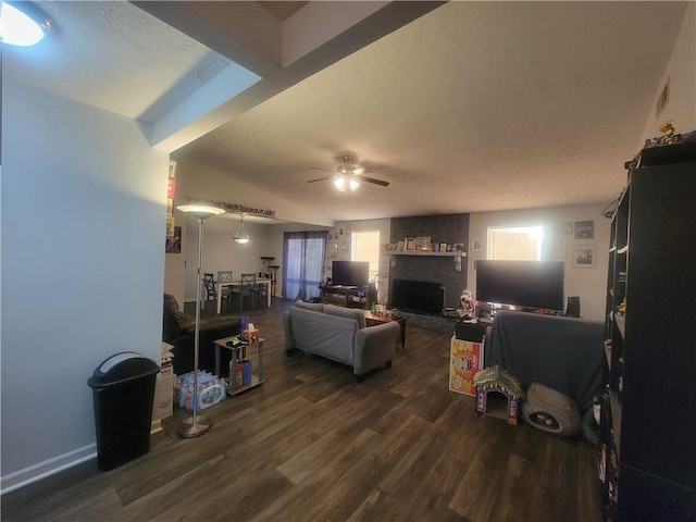 living area with ceiling fan, a wealth of natural light, dark wood finished floors, and a fireplace