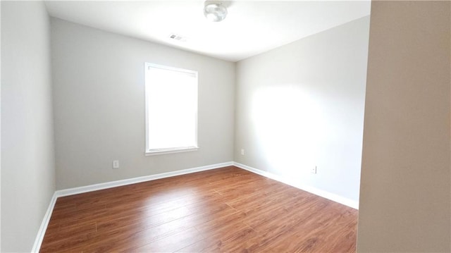 empty room with baseboards, wood finished floors, and visible vents