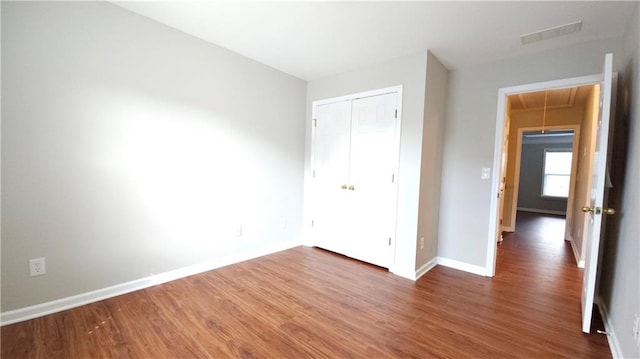 unfurnished bedroom with attic access, visible vents, wood finished floors, baseboards, and a closet