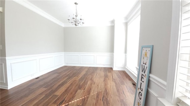 unfurnished dining area featuring visible vents, wood finished floors, a wainscoted wall, a notable chandelier, and ornamental molding