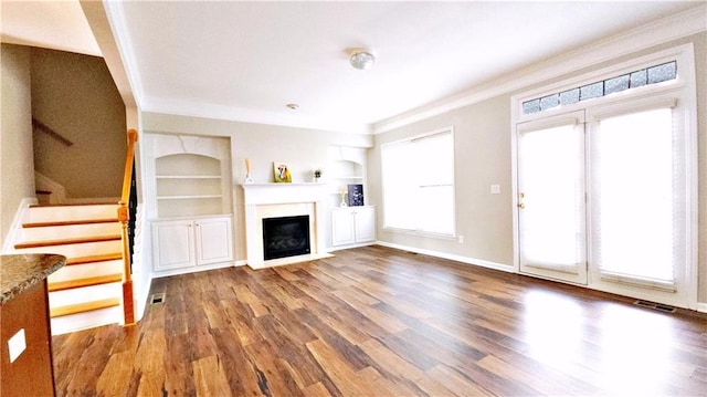 unfurnished living room featuring visible vents, built in features, wood finished floors, stairway, and ornamental molding