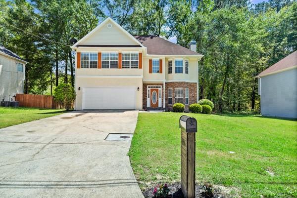 traditional-style house featuring concrete driveway, an attached garage, stucco siding, a chimney, and brick siding