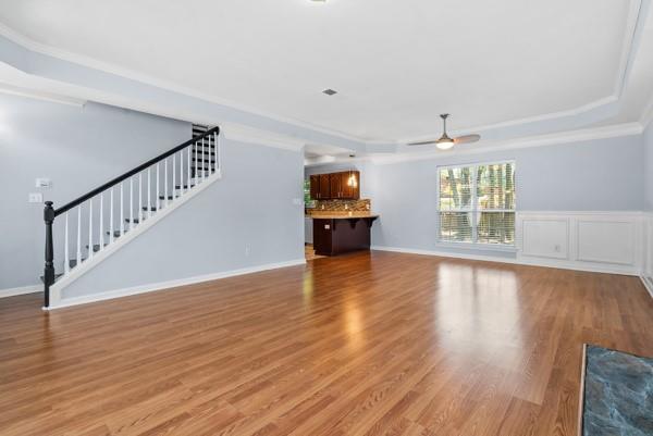 unfurnished living room with a tray ceiling, stairs, ceiling fan, light wood finished floors, and ornamental molding