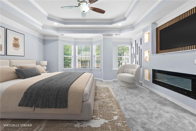bedroom with a raised ceiling, baseboards, crown molding, a glass covered fireplace, and carpet flooring