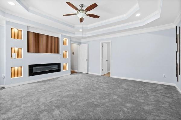 unfurnished living room with a raised ceiling, crown molding, a ceiling fan, carpet, and recessed lighting