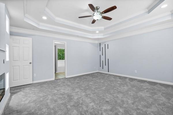 unfurnished bedroom featuring a tray ceiling, ornamental molding, carpet, recessed lighting, and baseboards