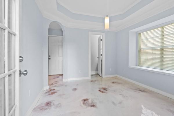 unfurnished bedroom featuring arched walkways, a raised ceiling, and baseboards