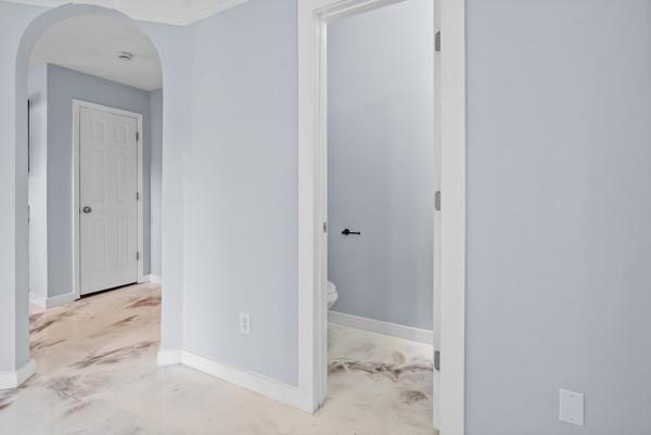 hallway featuring arched walkways, unfinished concrete floors, and baseboards