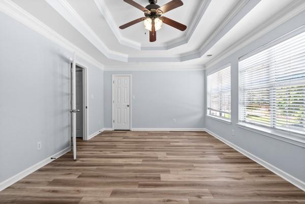 unfurnished bedroom with a tray ceiling, wood finished floors, crown molding, baseboards, and a ceiling fan