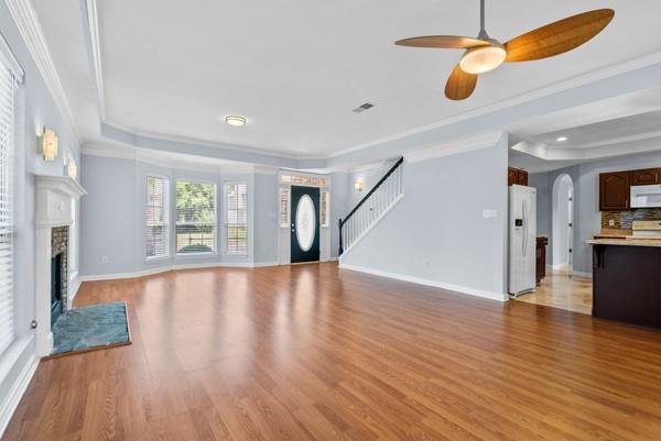 unfurnished living room featuring a raised ceiling, light wood-style flooring, ceiling fan, baseboards, and ornamental molding