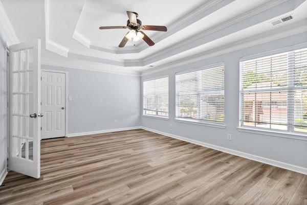 unfurnished bedroom with a tray ceiling, ornamental molding, wood finished floors, baseboards, and a ceiling fan