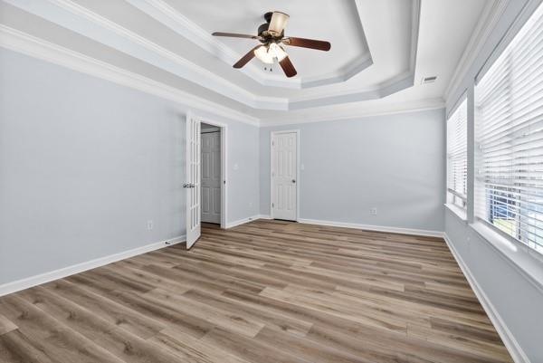 unfurnished bedroom with a tray ceiling, ornamental molding, wood finished floors, baseboards, and a ceiling fan