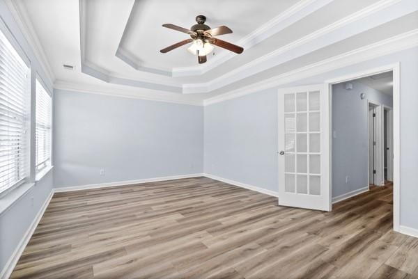 unfurnished room with a ceiling fan, a raised ceiling, wood finished floors, crown molding, and baseboards
